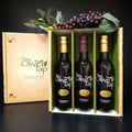 The Olive Tap Trio Gift Box from The Olive Tap: An Olive Tap gift box with three bottles inside and grapes on top of the box on a dark background and surface.