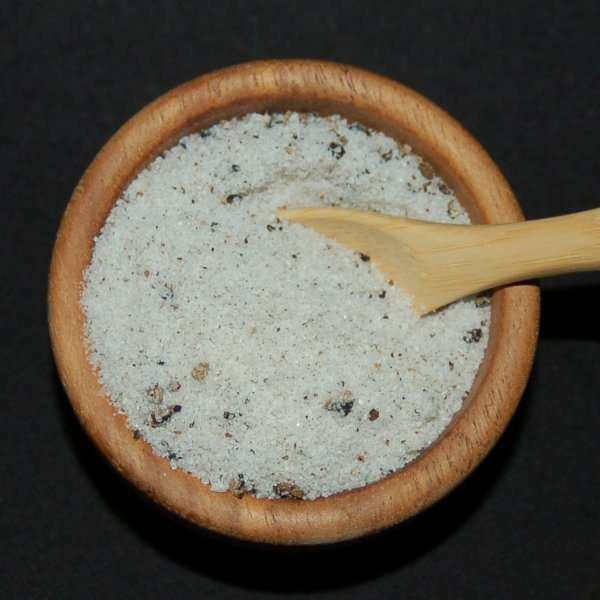Truffle Sea Salt by The Olive Tap: A wooden bowl and wooden spoon full of white sea salt with dark flakes mixed in against a black background.