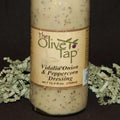 A glass bottle of Vidalia Onion & Peppercorn Dressing from The Olive Tap, surrounded by green decorative crinkle paper against a black background.