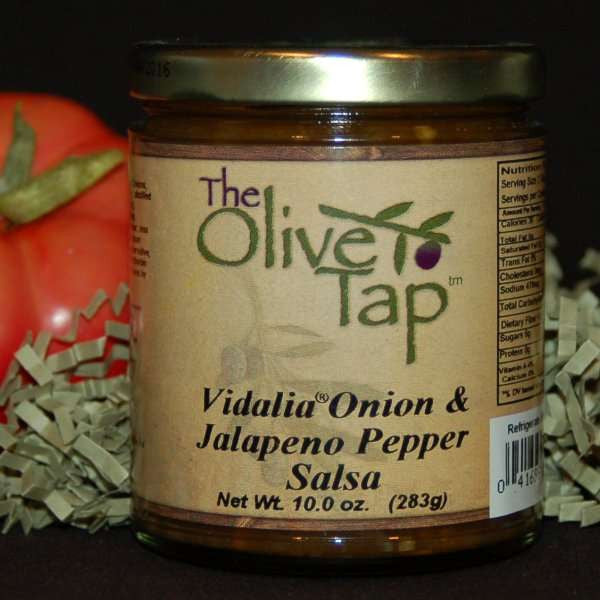 A jar of Vidalia Onion and Jalapeño Pepper Salsa from The Olive Tap surrounded by green decorative crinkle paper and a tomato against a black background and surface.