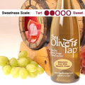 A bottle of Watermelon Rose White Balsamic Vinegar from The Olive Tap surrounded by grapes in front of a wooden barrel with a picture of sliced watermelon, and a sweetness scale indicating a two.