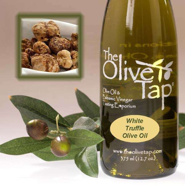 A bottle of White Truffle Olive Oil from The Olive Tap next to olives and leaves with an inset showing fresh truffles on a light background.