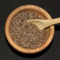 Applewood Smoked Sea Salt from The Olive Tap in a wooden bowl with pieces of brown sea salt and a wooden spoon in the bowl against a black background.