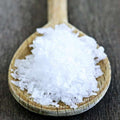 A wooden spoon filled with Kosher Flake Sea Salt from The Olive Tap on a wooden background.