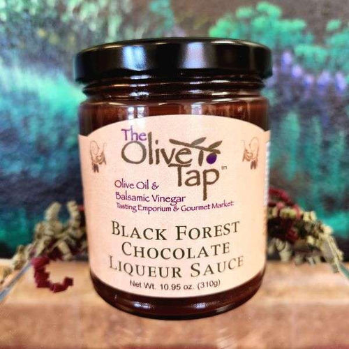 A jar of Black Forest Chocolate Liqueur Sauce from The Olive Tap with a colorful background and surrounded by red and green decorative crinkle paper.