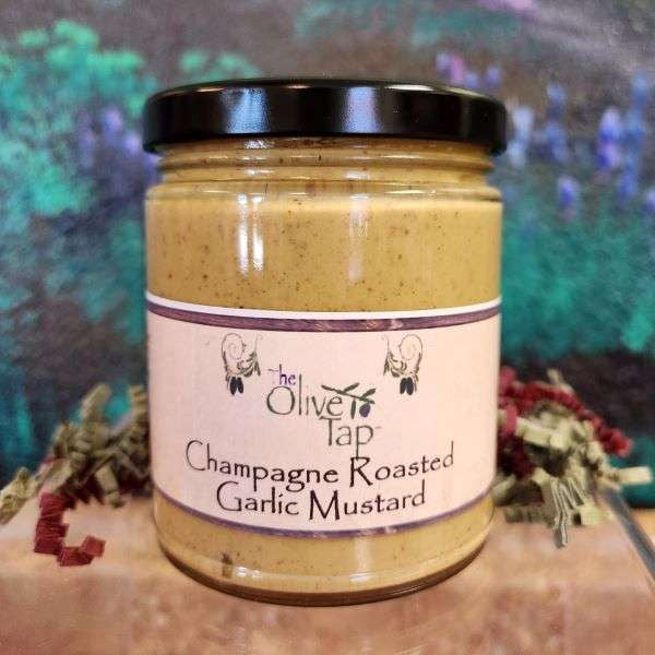 A jar of Champagne Roasted Garlic Mustard from The Olive Tap with a colorful background and surrounded by red and green decorative crinkle paper.