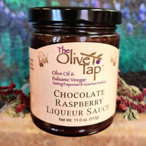 A jar of Chocolate Raspberry Liqueur Sauce from The Olive Tap with a colorful background and surrounded by red and green decorative crinkle paper.