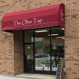 A brick wall with doors to enter The Olive Tap Crystal Lake store with a dark red awning with The Olive Tap