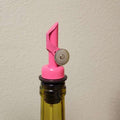 Limited Edition Pink Pour Spout from The Olive Tap inside the opening of a glass bottle in front of a white background.