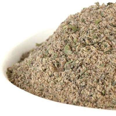 Greek Seasoning from The Olive Tap: A white bowl of ground green herbs with some chunks against a white background.
