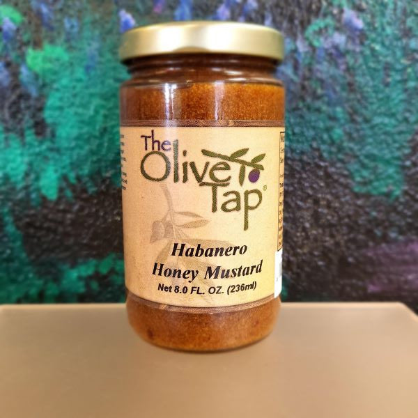 Habanero Honey Mustard from The Olive Tap in a glass jar with a turquoise, black, and purple background.