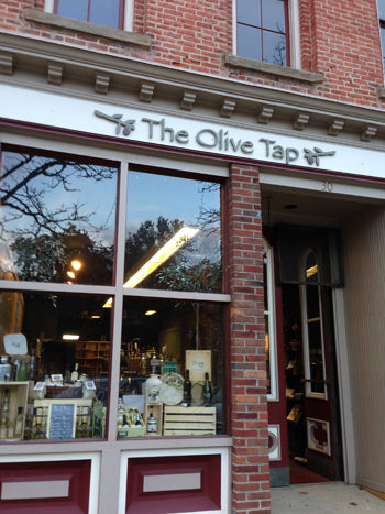 Storefront of 'The Olive Tap' with large glass window displaying items inside.