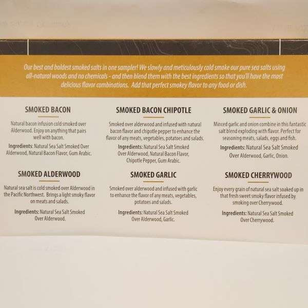 The Olive Tap's Smoked Sea Salt Sampler, back of the package: Six names of sea salt flavors in bold with their ingredients listed under each name, as well as a description of each smoked sea salt. A yellow band at the top of the picture that describes the sampler as a whole.