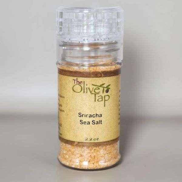 Sriracha Sea Salt in Grinder from The Olive Tap with a clear cap, The Olive Tap logo with an olive branch, against a white backdrop.