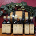 Vincotto Vinegar Variety of Bottles from The Olive Tap: Six bottles of vinegar in front of a decorative wooden barrel with leaves and a red background.